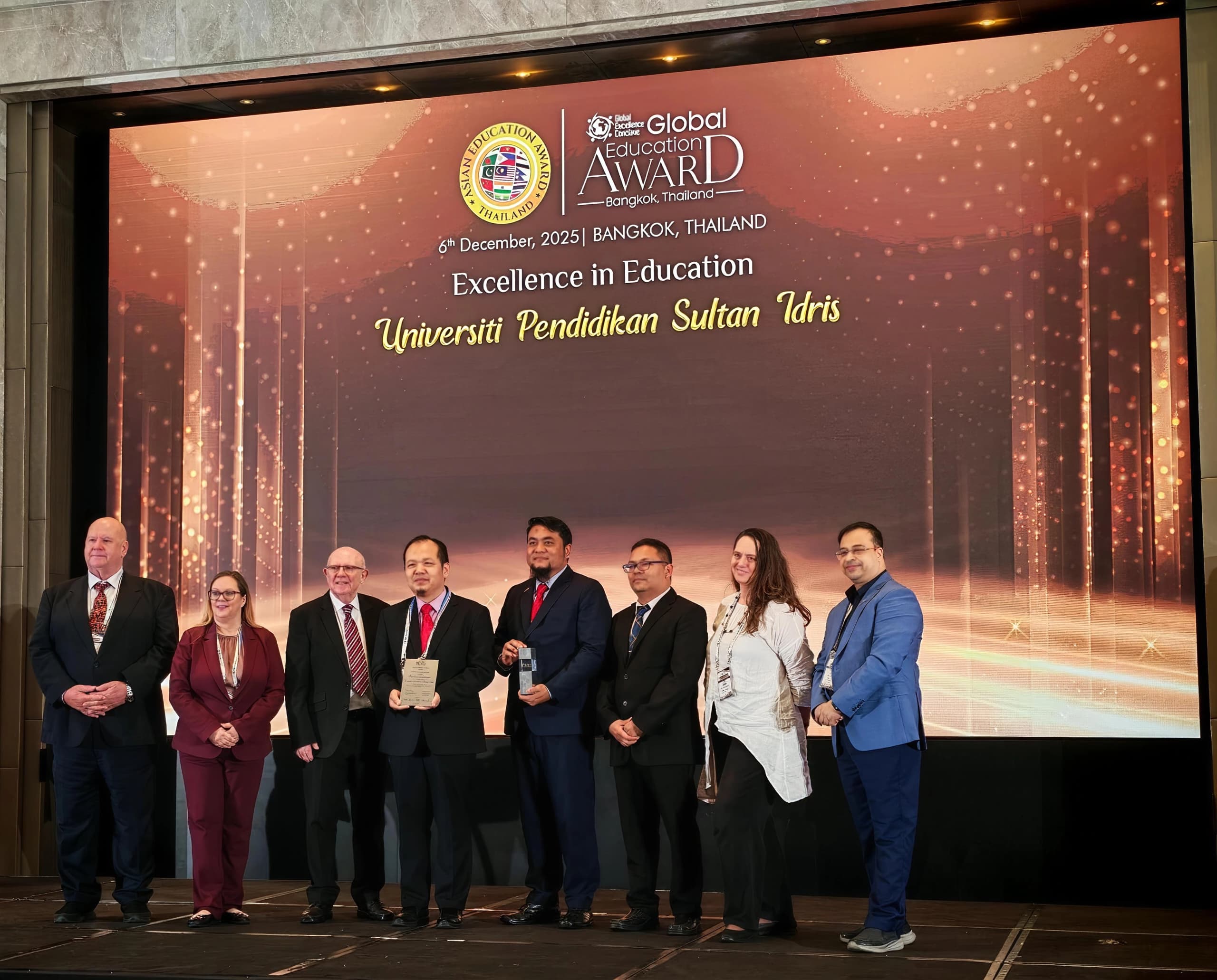 Prof. Madya Dr. Ridzwan (lima dari kanan) dan Prof. Dr. Mohd Izwan (empat dari kanan) bergambar sambil memegang plak anugerah berkenaan pada Global Education Award 2025 di Hotel Amari, Bangkok.